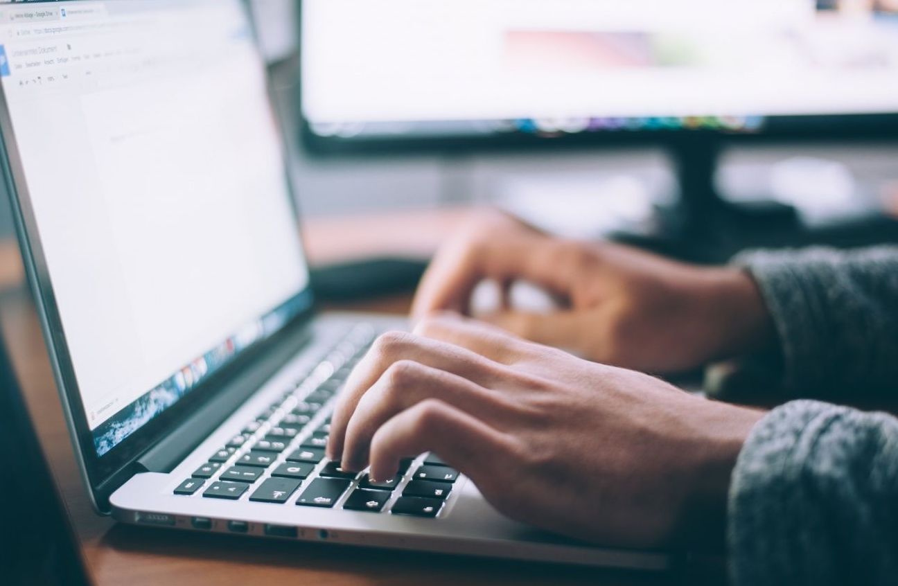 Mãos digitando em teclado de notebook com bordas arredondadas e detalhe verde
